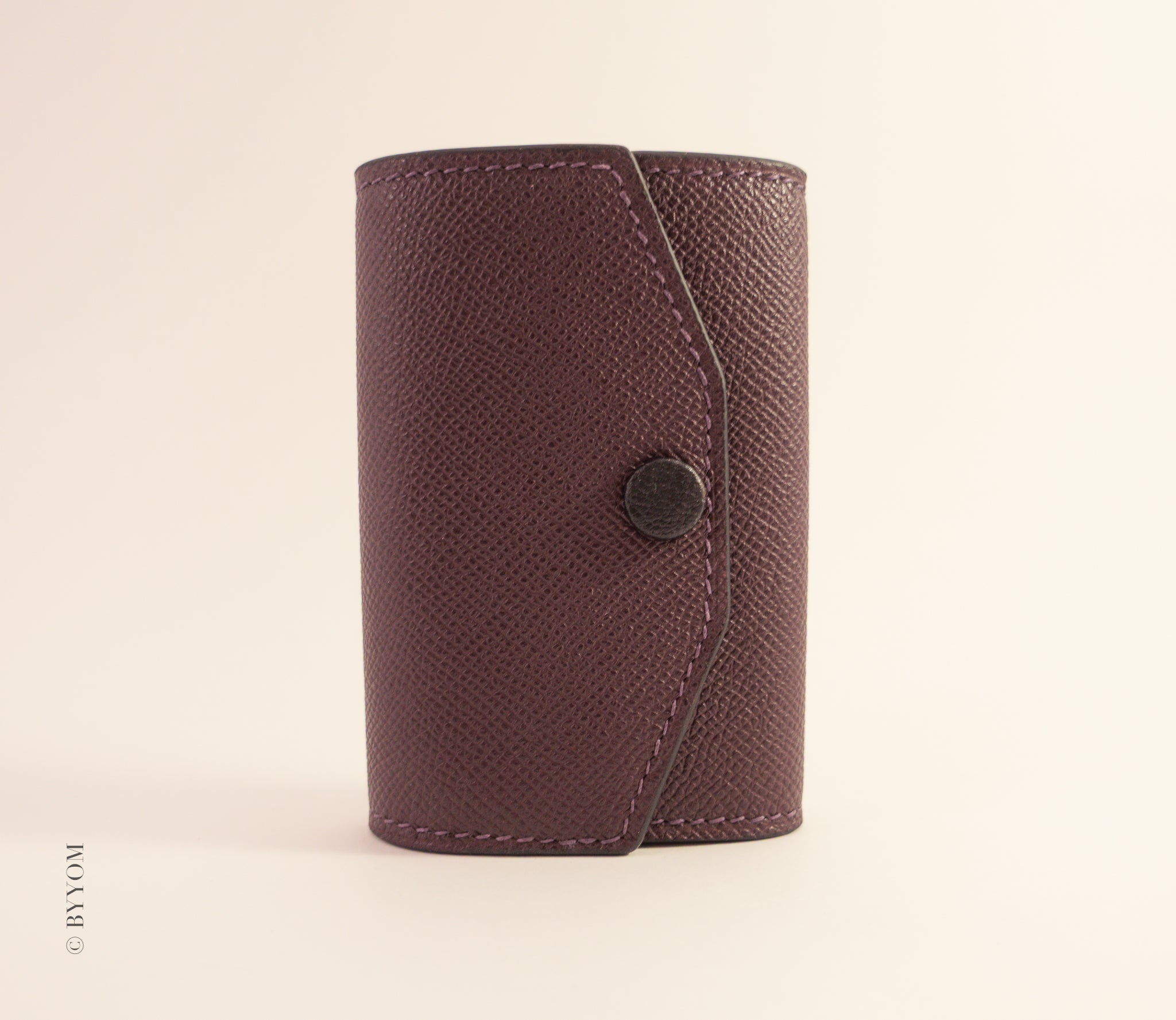 wine color leather wallet with a goat skin covered snap button on a beige background