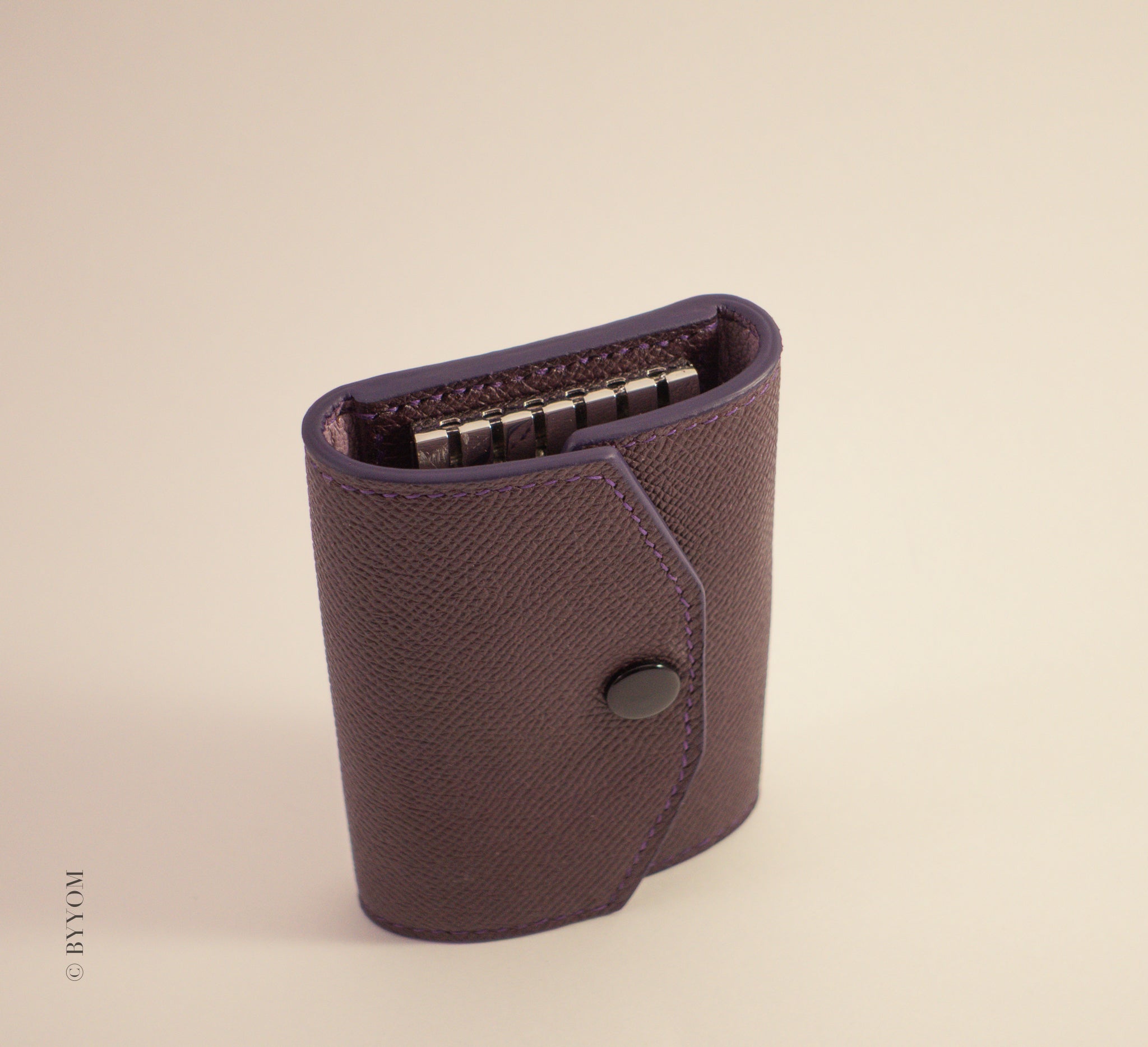 Epsom leather wallet with shiny black snap closure on a beige background