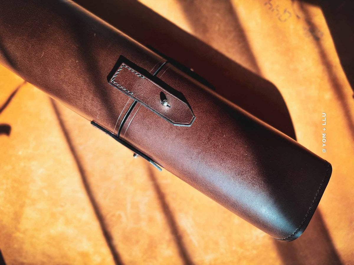 Close-up of a brown leather case with stitching detail on a textured brown background